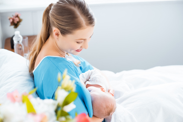 widok boczny szczęśliwą matką młodych piersią noworodka na łóżko w szpitalu  - Zdjęcie, obraz