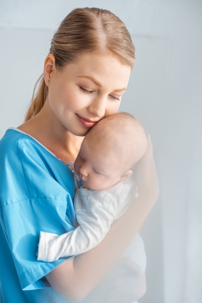 красивая счастливая молодая мама с закрытыми глазами обнимает очаровательного ребенка в больничной палате
 - Фото, изображение
