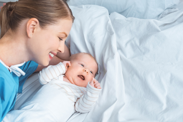 μεγάλη γωνία θέα ευτυχισμένη νεαρή μητέρα βλέπει αξιολάτρευτο μωρό ξαπλωμένη στο κρεβάτι - Φωτογραφία, εικόνα
