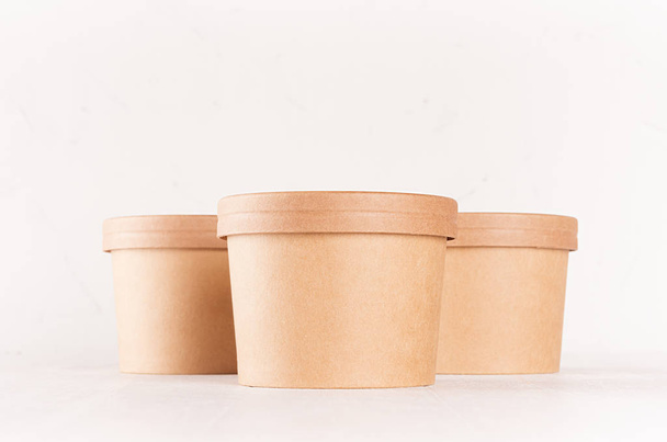 Set of three blank kraft paper bowls with caps for fast food on white wood table, closeup, food mockup for branding identity, advertising. - Φωτογραφία, εικόνα