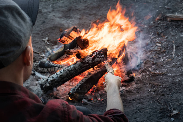 Lagerfeuer im Wald machen. Mann in Freizeitkleidung legt Holzstücke in brennendes Feuer. - Foto, Bild