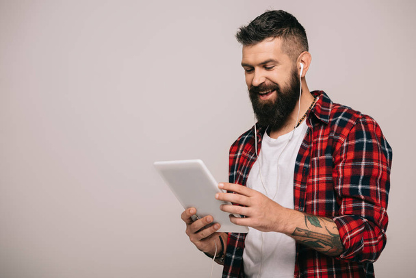 uśmiechający się Brodaty mężczyzna w kraciaste koszule z słuchawki za pomocą cyfrowego tabletu, na szarym tle - Zdjęcie, obraz
