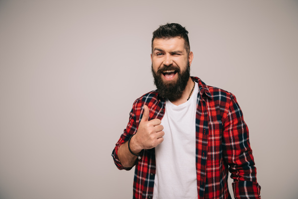 excited bearded man winking and showing thumb up, isolated on grey - Photo, Image