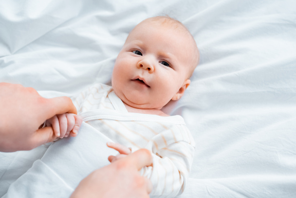 oříznuté shot matka držení rukou rozkošný kojenecké dítěte leží na bílé ložní prádlo - Fotografie, Obrázek