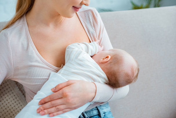 cropped shot of young woman breastfeeding infant daughter at home - Foto, Imagen
