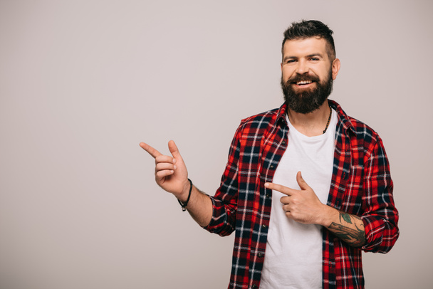 smiling bearded man in checkered shirt showing something isolated on grey   - Fotoğraf, Görsel