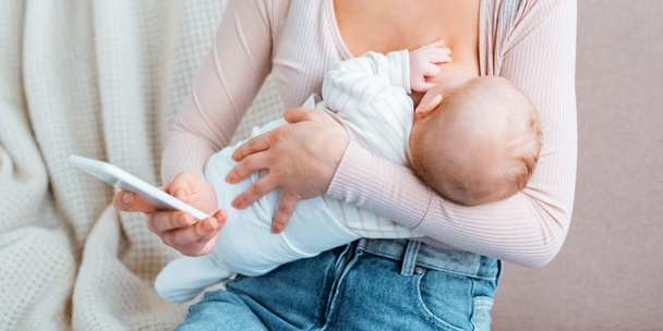 bijgesneden schot van jonge moeder en baby borstvoeding en gebruik van de smartphone - Foto, afbeelding