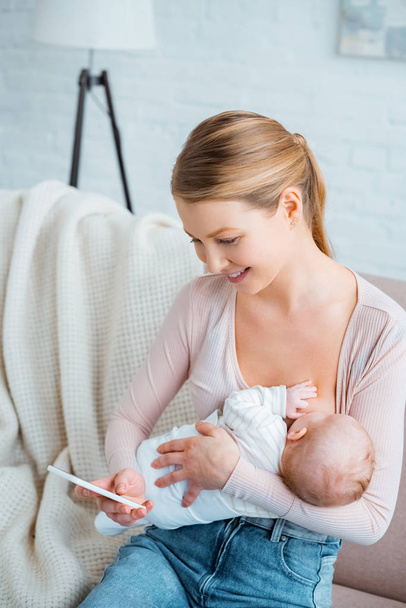 high angle view of happy young mother breastfeeding baby and using smartphone at home - Fotografie, Obrázek