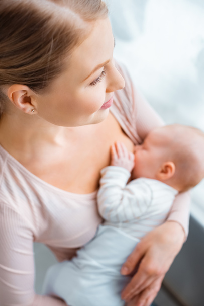 visão de alto ângulo de sorrir jovem mãe amamentando bebê em casa
 - Foto, Imagem