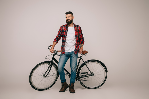 happy man in checkered shirt posing with bicycle on grey - Photo, Image
