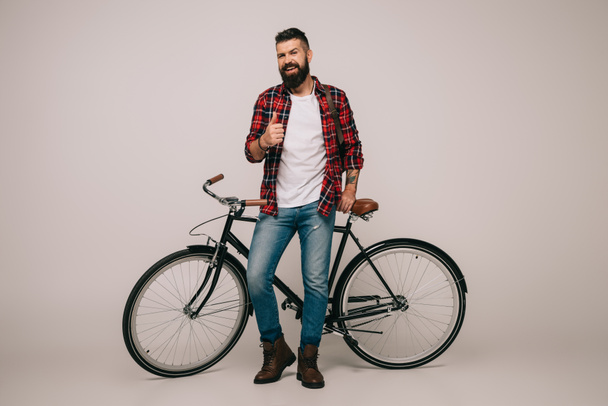 bel homme souriant en chemise à carreaux posant avec vélo et montrant pouce vers le haut sur gris
 - Photo, image