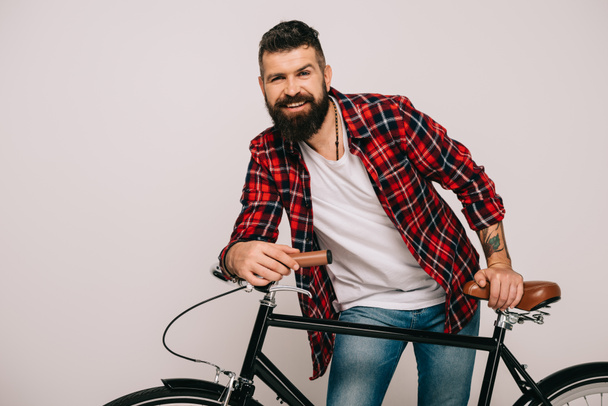 handsome bearded smiling man posing with bicycle isolated on grey - Foto, Imagen
