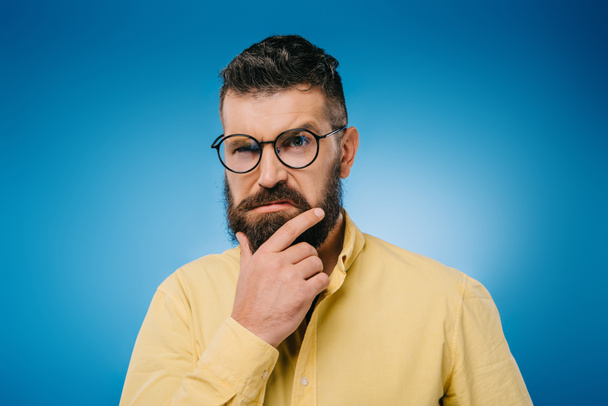 Verdächtiger bärtiger Mann mit Brille isoliert auf blauem Grund - Foto, Bild