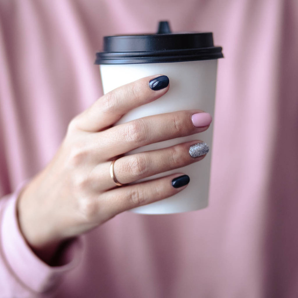 Gorgeous manicure, pastel tender pink color nail polish, closeup photo. Female hands hold a plastic coffee cup over simple background - Photo, Image