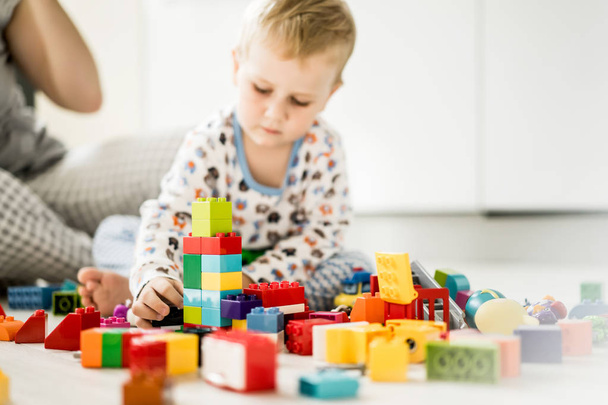 boy child playing with his mother in color children's building kit. The details of the children's building kit are scattered on the floor. - Φωτογραφία, εικόνα