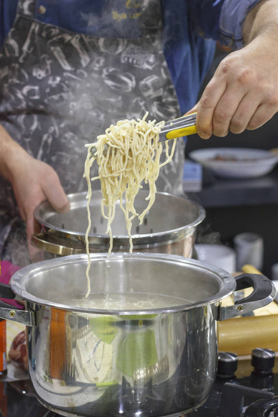 Chef takes out with slotted spoon hot steaming egg noodles from pan - Photo, Image