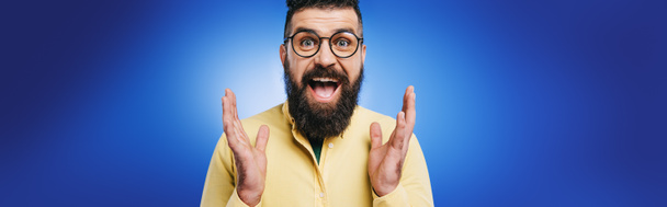 excited handsome man in eyeglasses gesturing isolated on blue - Photo, Image