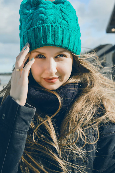 mooie blonde meisje met blauwe ogen en lange haren in een close-up portret van warme groene gebreide muts - Foto, afbeelding