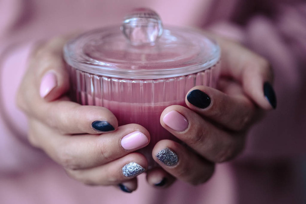 Gorgeous manicure, pastel tender pink color nail polish, closeup photo. Female hands hold a candle over simple background - 写真・画像