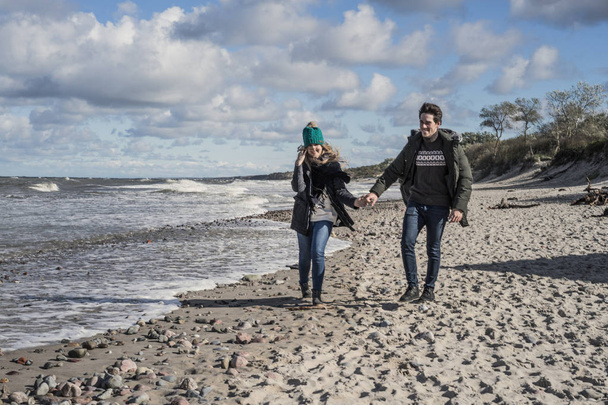 a young couple in love spending weekends on the coast of the cold Baltic sea, sandy beach, warm jackets, family weekend man and woman running on the beach. - Photo, image