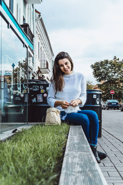 beautiful brunette girl with long hair is engaged in knitting in a city cafe, favorite hobby knitting on knits - Фото, изображение