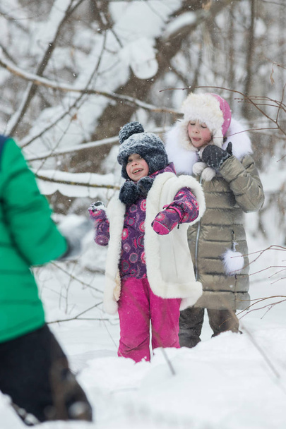 Foresta invernale. Due bambine che giocano a palle di neve con un amico
 - Foto, immagini
