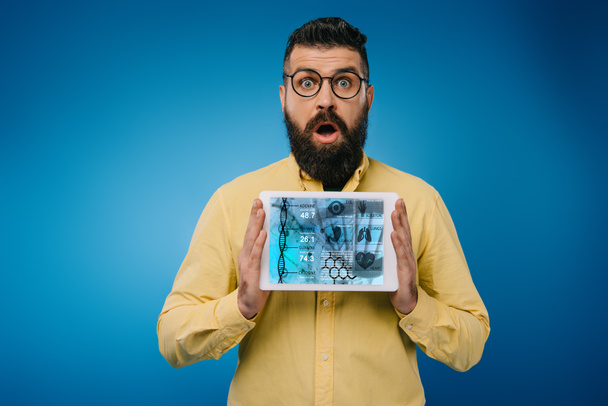 shocked bearded man presenting digital tablet with dna app, isolated on blue - Foto, immagini