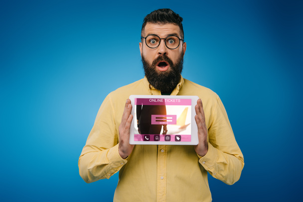 shocked bearded man presenting digital tablet with online tickets app, isolated on blue - Photo, Image