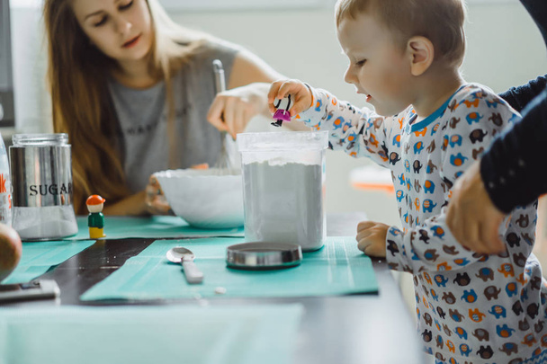 menino criança de pijama de manhã com a mãe cozinhar torta de maçã na cozinha e brincar com brinquedos - Foto, Imagem