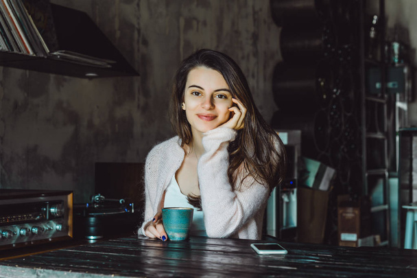 a beautiful brunette girl with a charming smile and expressive brown eyes drinking coffee and using a smartphone - Photo, image