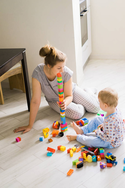 jongen kind spelen met zijn moeder in kleur kinderen bouwpakket. De details van de bouwpakket voor kinderen zijn verspreid over de vloer. - Foto, afbeelding