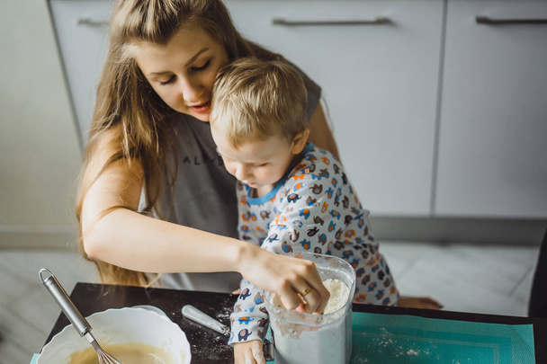 niño niño en pijama por la mañana con mamá cocinando pastel de manzana en la cocina y jugando con juguetes - Foto, Imagen
