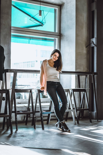 beautiful brunette girl with a charming smile and expressive brown eyes drinking coffee in a cafe with an interior in loft style - 写真・画像