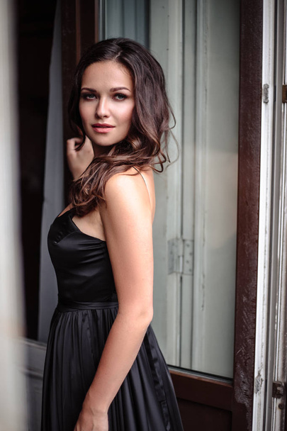 Portrait of young woman in elegant silk black dress posing in a dark interior, fashion beauty photo - 写真・画像