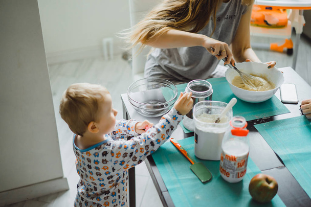 jongen kind in pyjama 's in de ochtend met mam koken appeltaart in de keuken en spelen met speelgoed - Foto, afbeelding