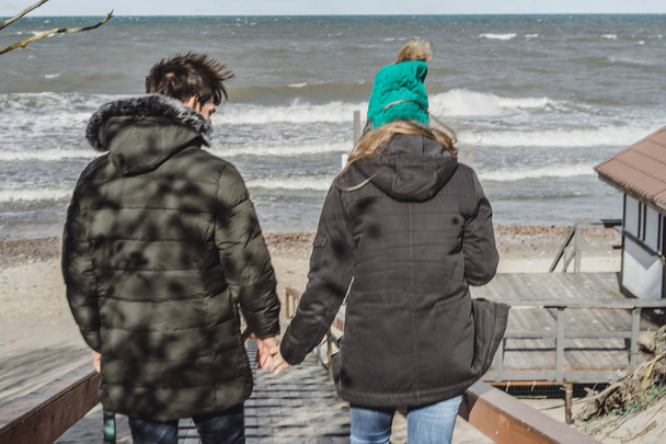 a young couple in love spending weekends on the coast of the cold Baltic sea, sandy beach, warm jackets, family weekend man and woman running on the beach. - Foto, afbeelding