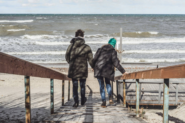 a young couple in love spending weekends on the coast of the cold Baltic sea, sandy beach, warm jackets, family weekend man and woman running on the beach. - Photo, image