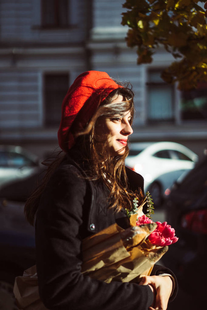 beautiful French woman brunette in a red beret with a bouquet of flowers and French baguettes under her arm walks through the park in Paris in a European city, in Paris - Foto, Bild