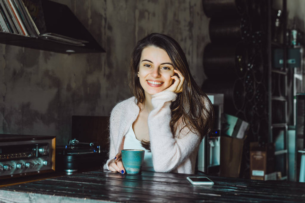 a beautiful brunette girl with a charming smile and expressive brown eyes drinking coffee and using a smartphone - Foto, imagen