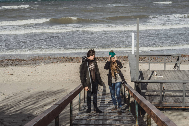 a young couple in love spending weekends on the coast of the cold Baltic sea, sandy beach, warm jackets, family weekend man and woman running on the beach. - Photo, Image