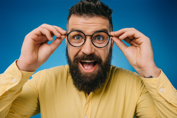 excited bearded man in eyeglasses isolated on blue - Foto, imagen