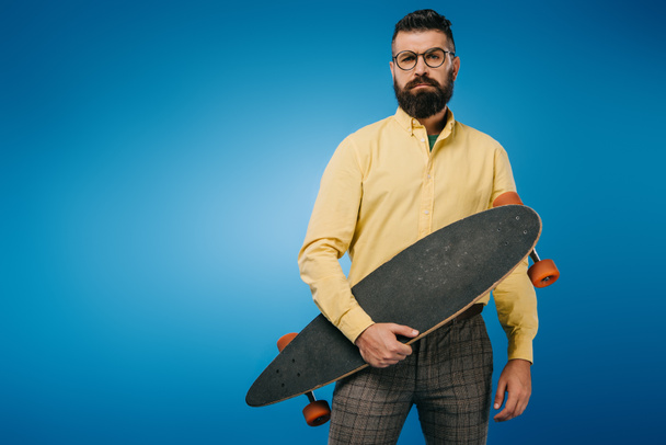 handsome bearded man holding longboard isolated on blue - Фото, изображение