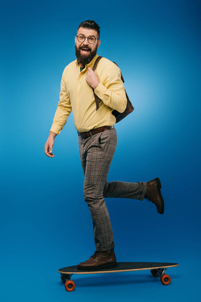 excited bearded man skateboarding in studio on blue - Photo, image