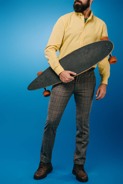 cropped view of man holding skateboard isolated on blue - Valokuva, kuva