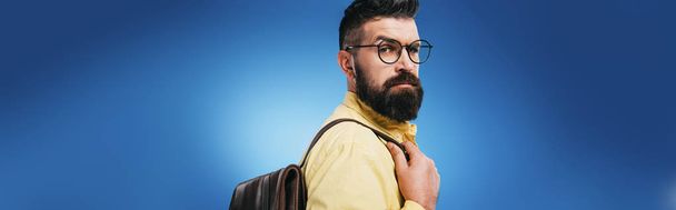 serious handsome man with backpack, isolated on blue - Photo, image
