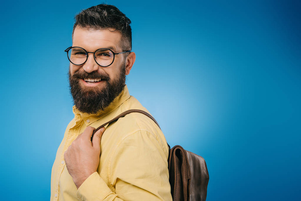 cheerful bearded man with backpack, isolated on blue - Фото, изображение