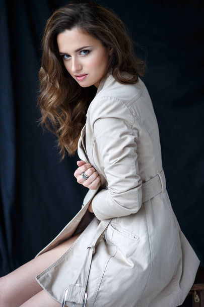 Fashion beauty portrait of young brunette woman in a trench coat in a simple interior - Photo, image
