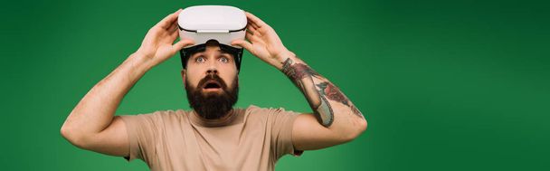 shocked bearded man with Virtual reality headset isolated on green - Foto, afbeelding