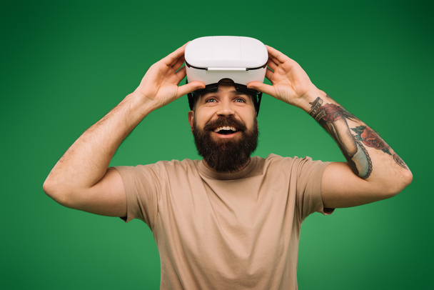 excited bearded man with Virtual reality headset isolated on green - Fotó, kép