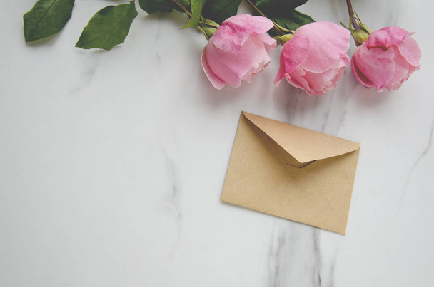 Pink roses and a craft envelope on marble table.Concept of greeting - Photo, Image